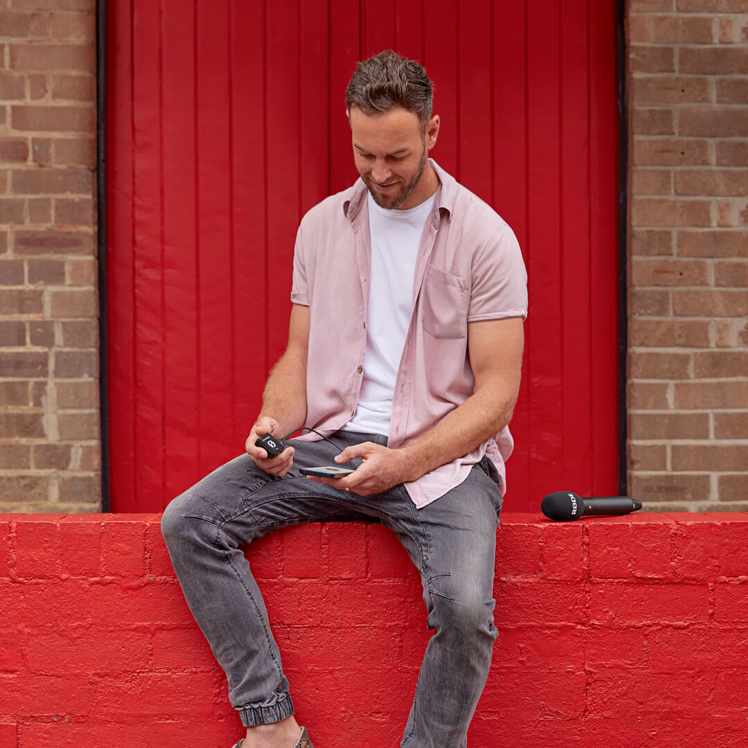 Man sitting on brick fence holding Wireless ME and mobile phone with Interview PRO next to him